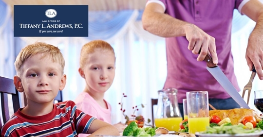 Two children sitting at table with man cutting food in background.