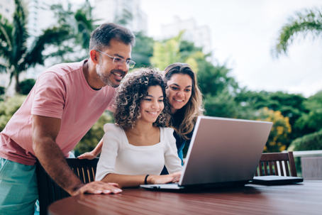 parents and teen daughter looking at a laptop