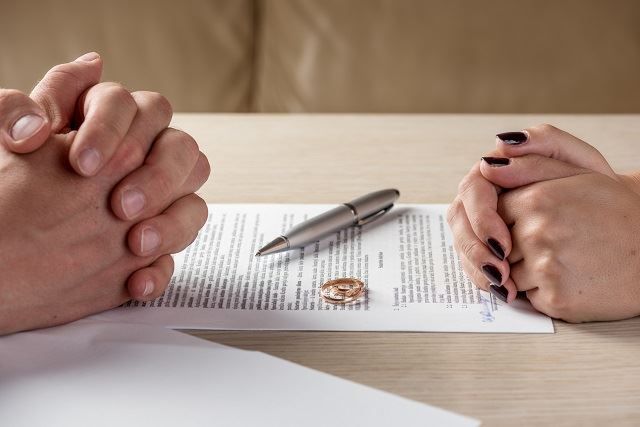 A couple's folded hand on either side of the table with legal separation paperwork between them